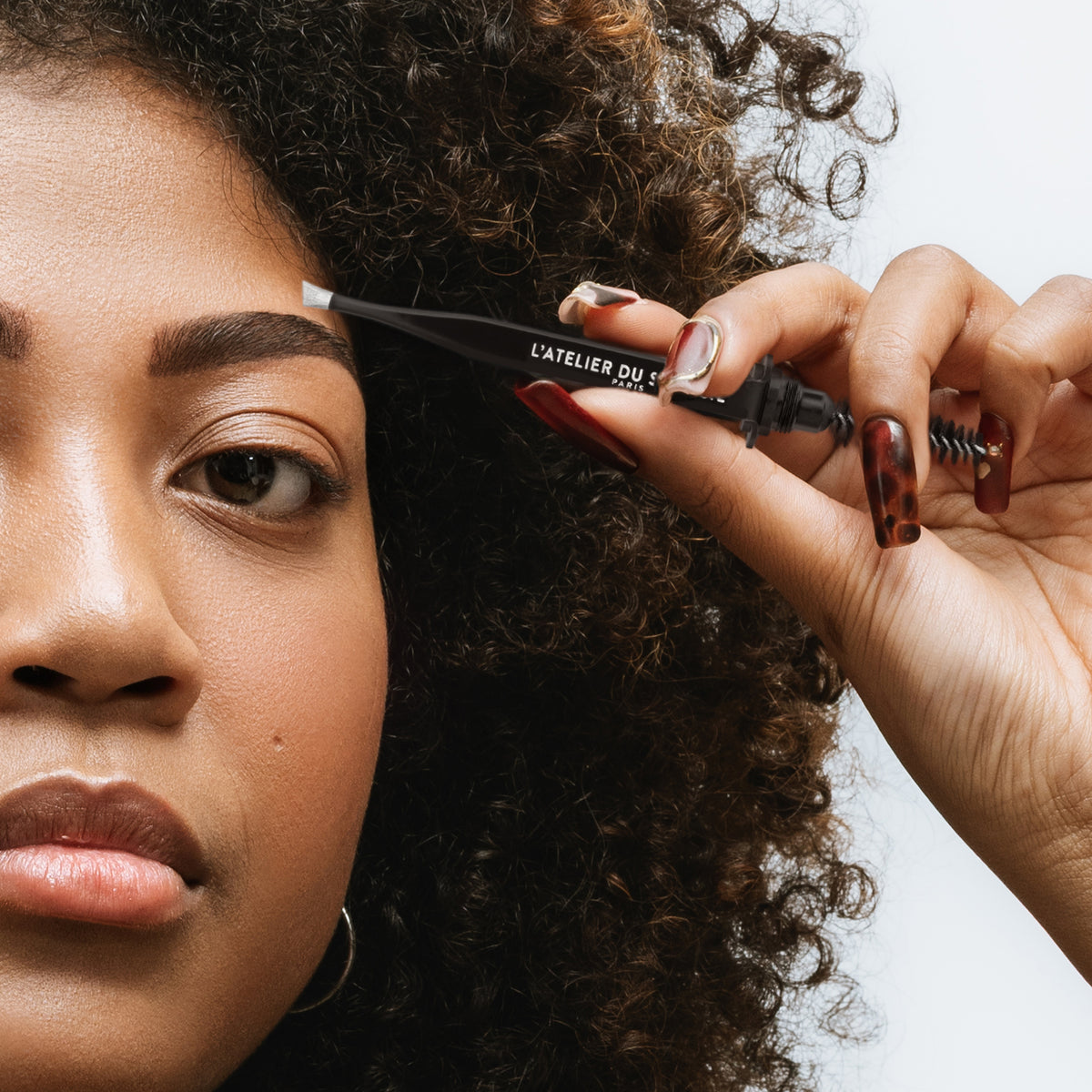 Épilation du bout du sourcil avec le Stylbrow+ par une modèle aux cheveux bouclés, pince à épiler L'Atelier du Sourcil